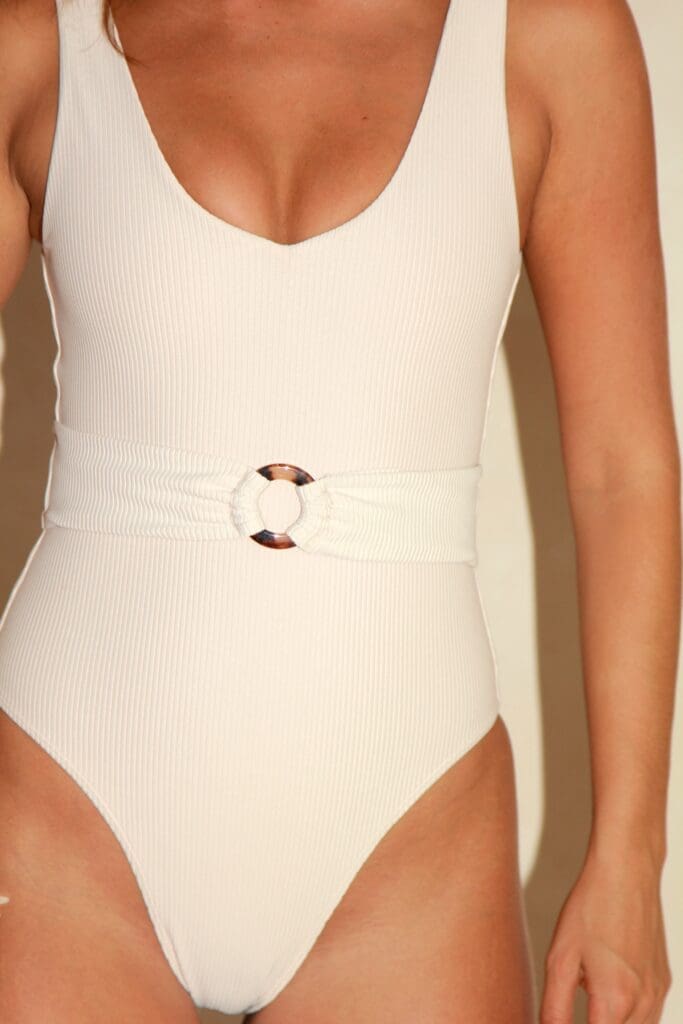 A woman wearing a white swimsuit with a belt around her waist.